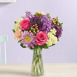 Mixed pink, purple, and cream flowers in a clear glass vase