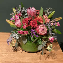 Pink and red mixed flower arrangement in a green bowl vase
