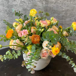 Mixed bouquet of yellow, peach, and pink flowers in a white vase