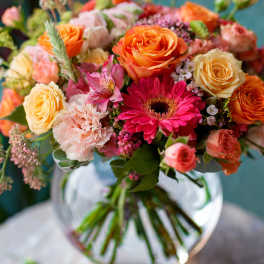 Mixed bouquet of orange, pink, and cream flowers in a glass vase