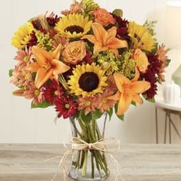 Bouquet of sunflowers, orange lilies, and roses in a glass vase