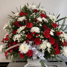 Red carnations and white daisies in a white container with a silver ribbon