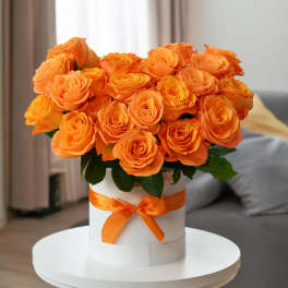 Orange roses arranged in a white hat box with an orange ribbon