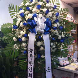 Large standing floral wreath with blue and white flowers and ribbon