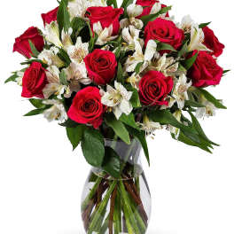 Red roses and white alstroemeria arranged in a clear glass vase