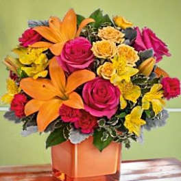Bright bouquet of orange lilies, pink roses, and yellow flowers in a square vase