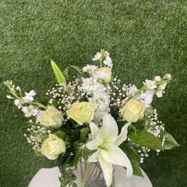 Bouquet of pale yellow roses and white lilies in a square glass vase