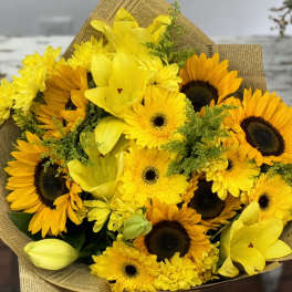 Bouquet of yellow sunflowers and lilies wrapped in newspaper-style paper