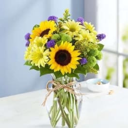 Sunflowers and yellow daisies in a clear glass vase with a twine bow
