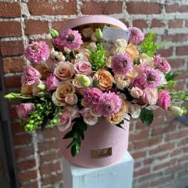 Arrangement of pink and peach roses with pink blooms in a round pink hatbox container