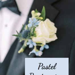 Pastel boutonniere with white rose and small blue flowers pinned to a black tuxedo lapel