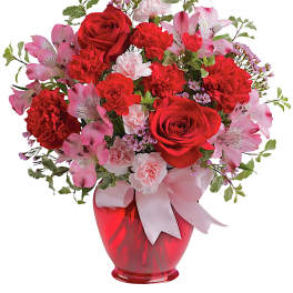 Red roses and pink flowers arranged in a red vase with a ribbon