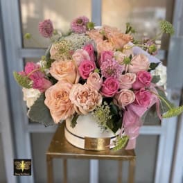 Peach and pink roses arranged in a white hatbox on a gold stand
