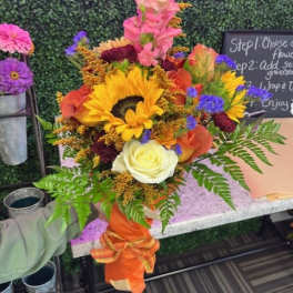 Bright mixed bouquet with sunflowers, roses, and snapdragons in an orange wrap