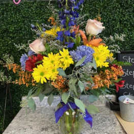 Colorful mixed flower arrangement in a glass vase with a purple ribbon