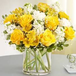 Yellow roses and white flowers arranged in a clear glass vase