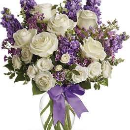 White roses and purple flowers in a glass vase with a purple ribbon
