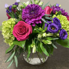 Bouquet of pink roses, purple blooms, and green hydrangeas in a glass vase