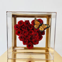 Heart-shaped red rose arrangement in a clear box with a butterfly accent