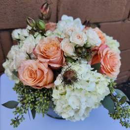 Low arrangement of peach roses, cream spray roses, and white hydrangeas in a round vase