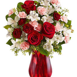 Red roses, white lilies, and pink carnations in a red glass vase