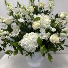 White floral arrangement in a white vase with roses, hydrangeas, and snapdragons