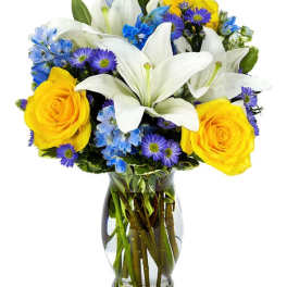 Bouquet of white lilies, yellow roses, and blue flowers in a glass vase