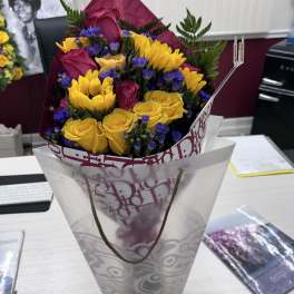 Bouquet of yellow and magenta roses with purple filler flowers in a gift wrap
