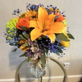 Bouquet of orange lilies, roses, and blue filler flowers in a glass vase
