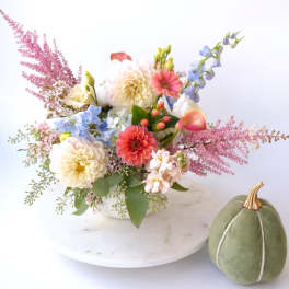 Mixed pastel flower arrangement in a white bowl with a green velvet pumpkin