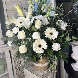 White floral arrangement with lilies, roses, and daisies in a woven vase