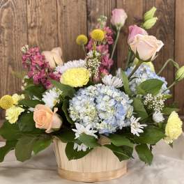 Mixed bouquet in a wooden basket with roses, hydrangea, and daisies