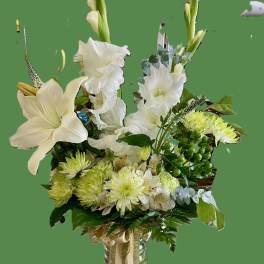 White floral arrangement in a glass vase with tall stems and green accents