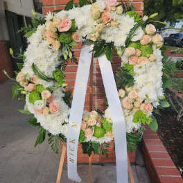 Standing wreath of white mums and peach roses with ribbon on wooden easel