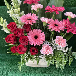 Pink gerbera daisies, red roses, and pink carnations in a white container