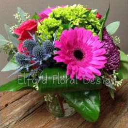 Bright mixed bouquet with pink gerbera daisies and blue thistle in a glass vase