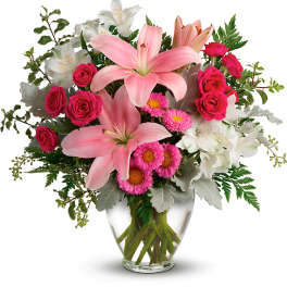 Pink lilies and roses in a clear glass vase with white flowers