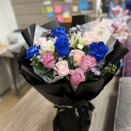 Bouquet of blue and pink roses with small purple flowers in black wrap