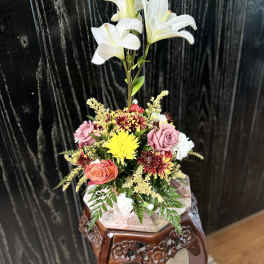 Arrangement of white lilies, roses, and chrysanthemums in a decorative container