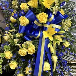 Yellow roses and lilies with blue flowers and a blue ribbon