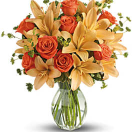 Orange roses and pale lilies in a clear glass vase