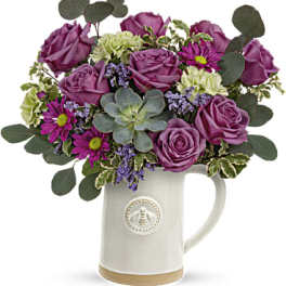 Purple roses and mixed flowers arranged in a white ceramic pitcher