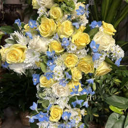 Tall floral spray of yellow and white roses with blue accent flowers