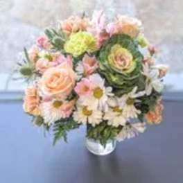 Round bouquet of peach roses, white daisies, and green ornamental blooms in a glass vase