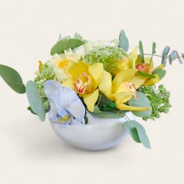 Yellow and pale blue orchids arranged in a white bowl vase