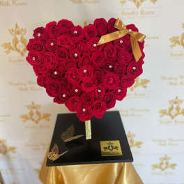 Heart-shaped red rose arrangement on a black stand with a gold bow