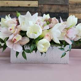 Pastel floral arrangement with white lilies and pale pink orchids in a rectangular container
