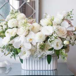 White floral arrangement in a ribbed white vase with pale pink accents