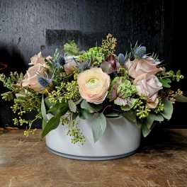 Low floral arrangement in a white container with pale roses and mixed blooms