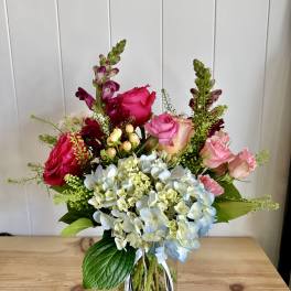 Mixed bouquet of roses, hydrangeas, and snapdragons in a glass vase